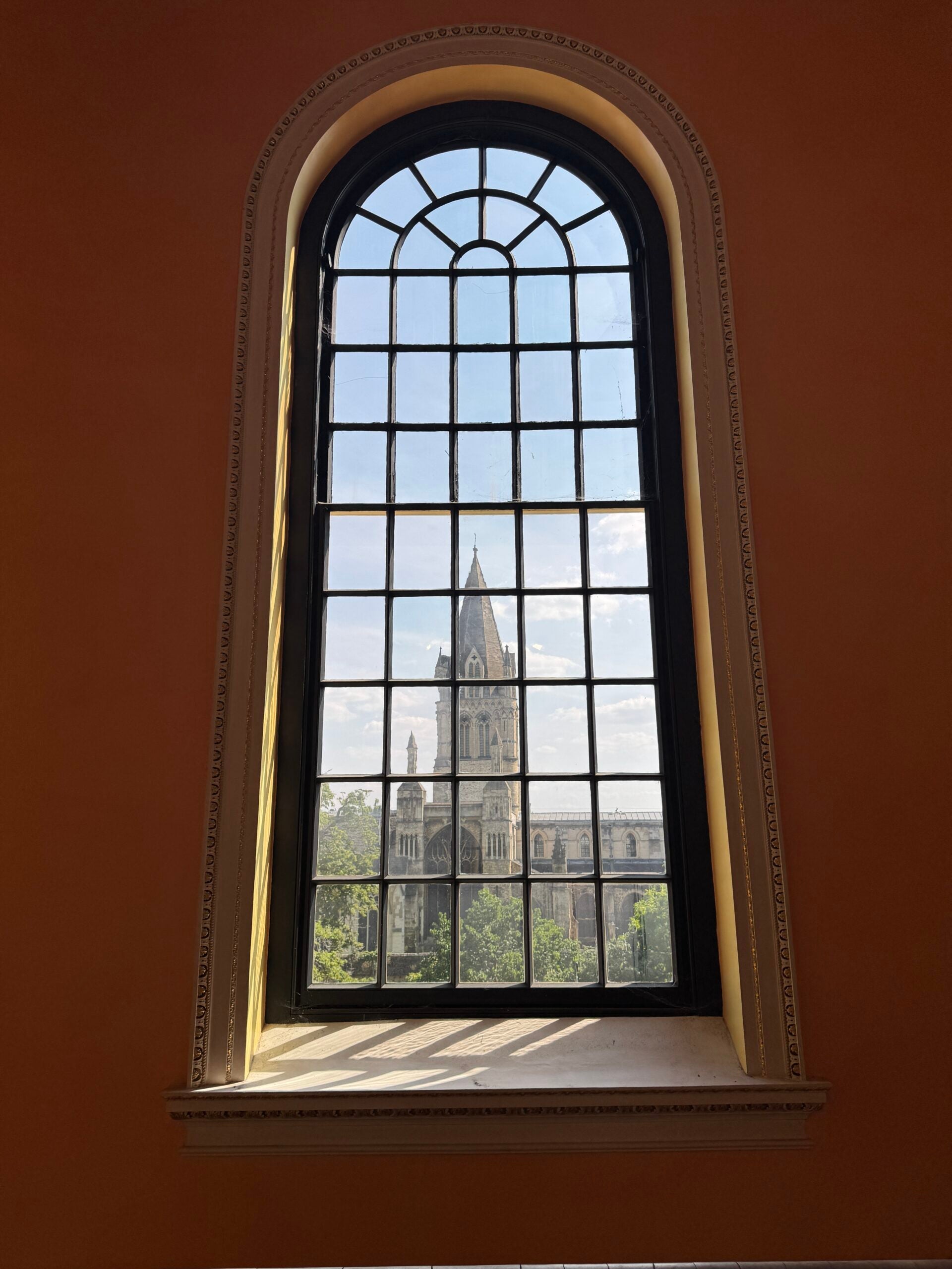 Red wall with an arched window with a view of a tall gothic building.