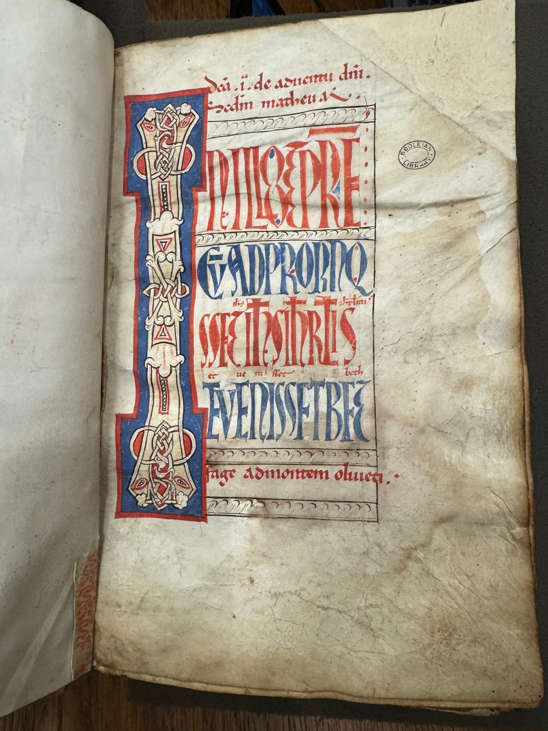 Folio title page with blue and red text and illustration on wrinkled yellow paper.