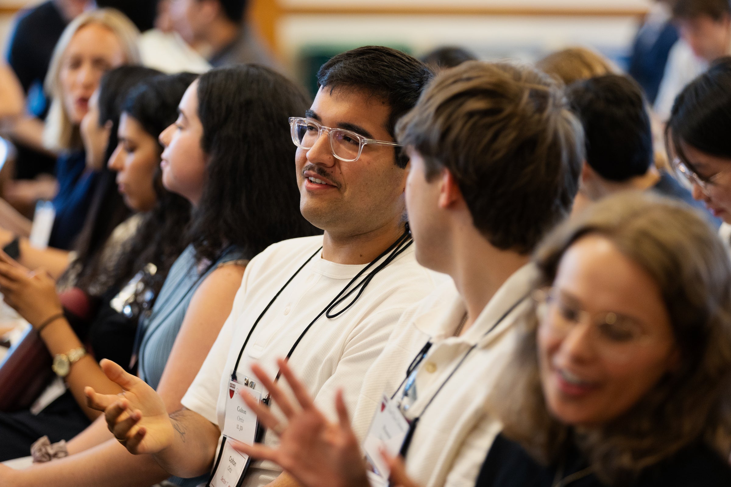 A group of students attending an event are seated in an audience and chatting with each other.