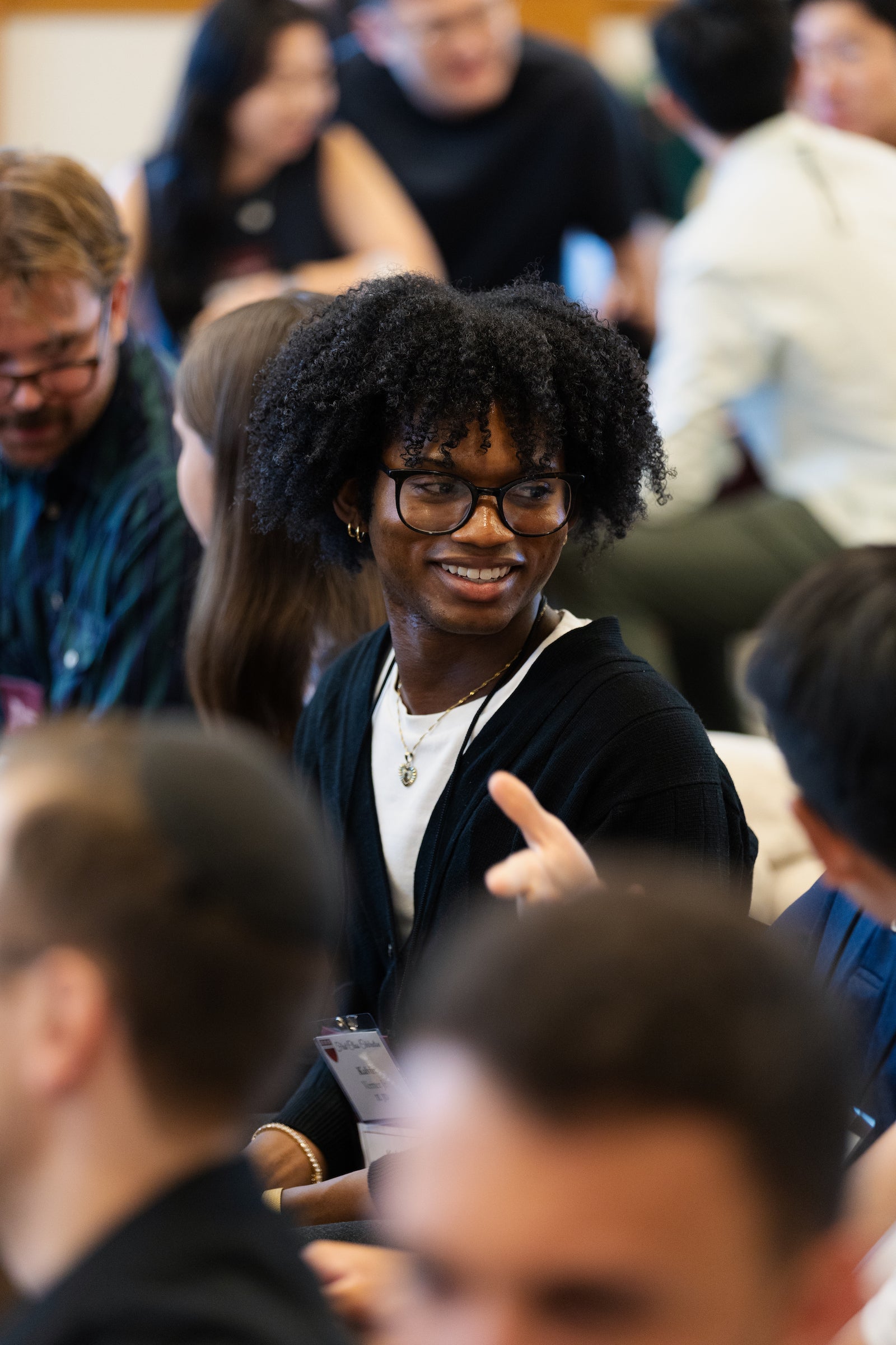 A student smile and converses with another while seated in an audience at an event.