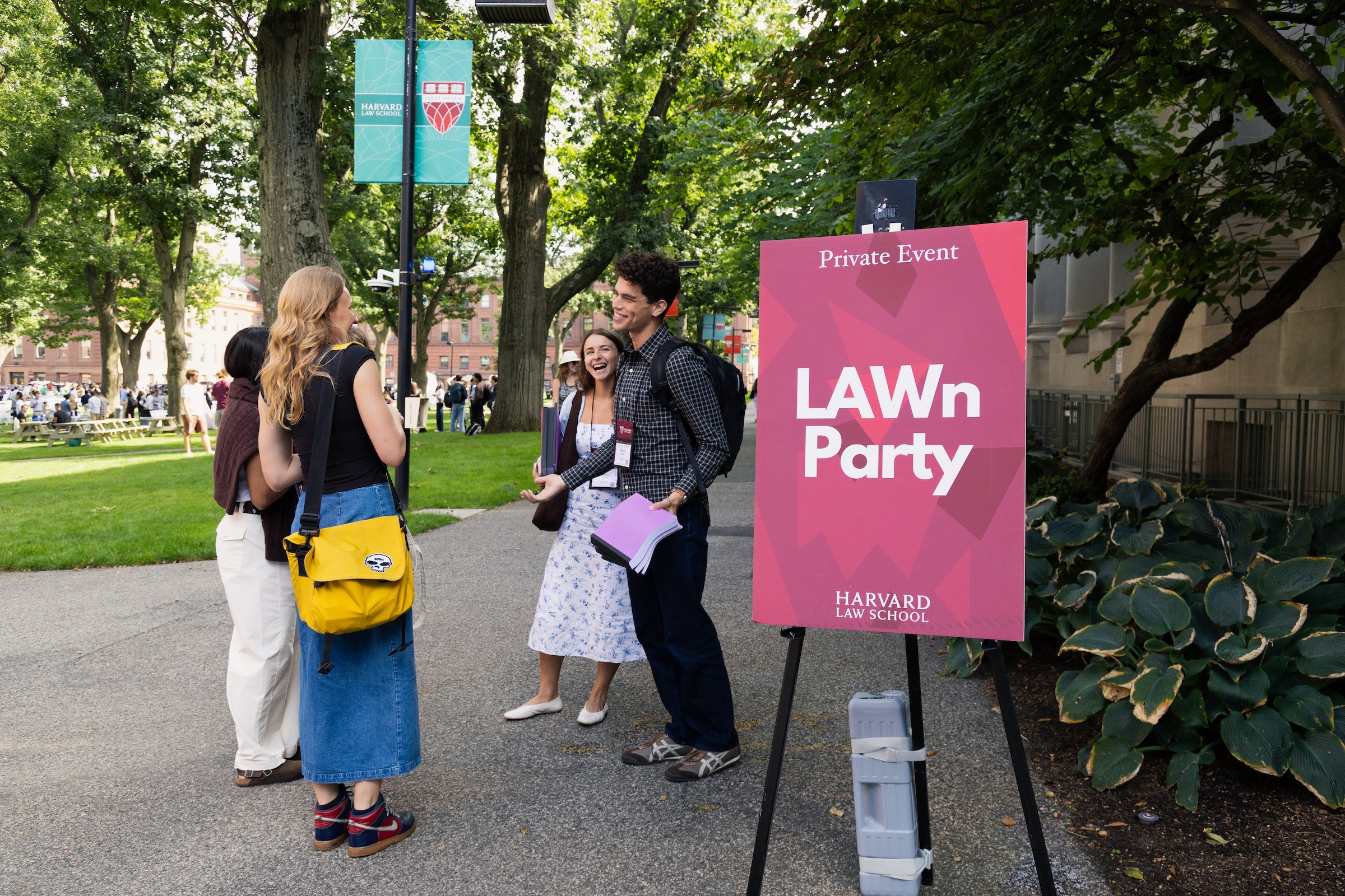 Students laugh together at an outdoor event behind a sign that says 