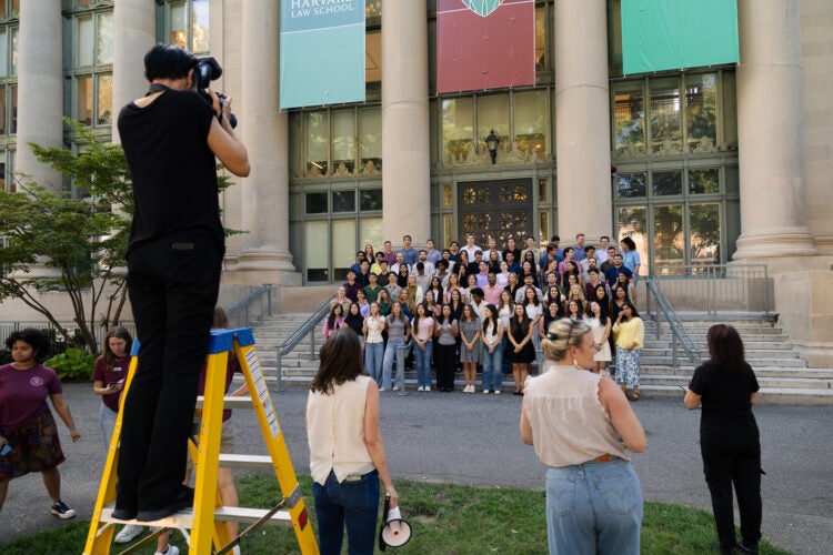 Students gather for a photograph on the steps of Langdell Hall. A photographer stands on a yellow stepladder to take a photograph.