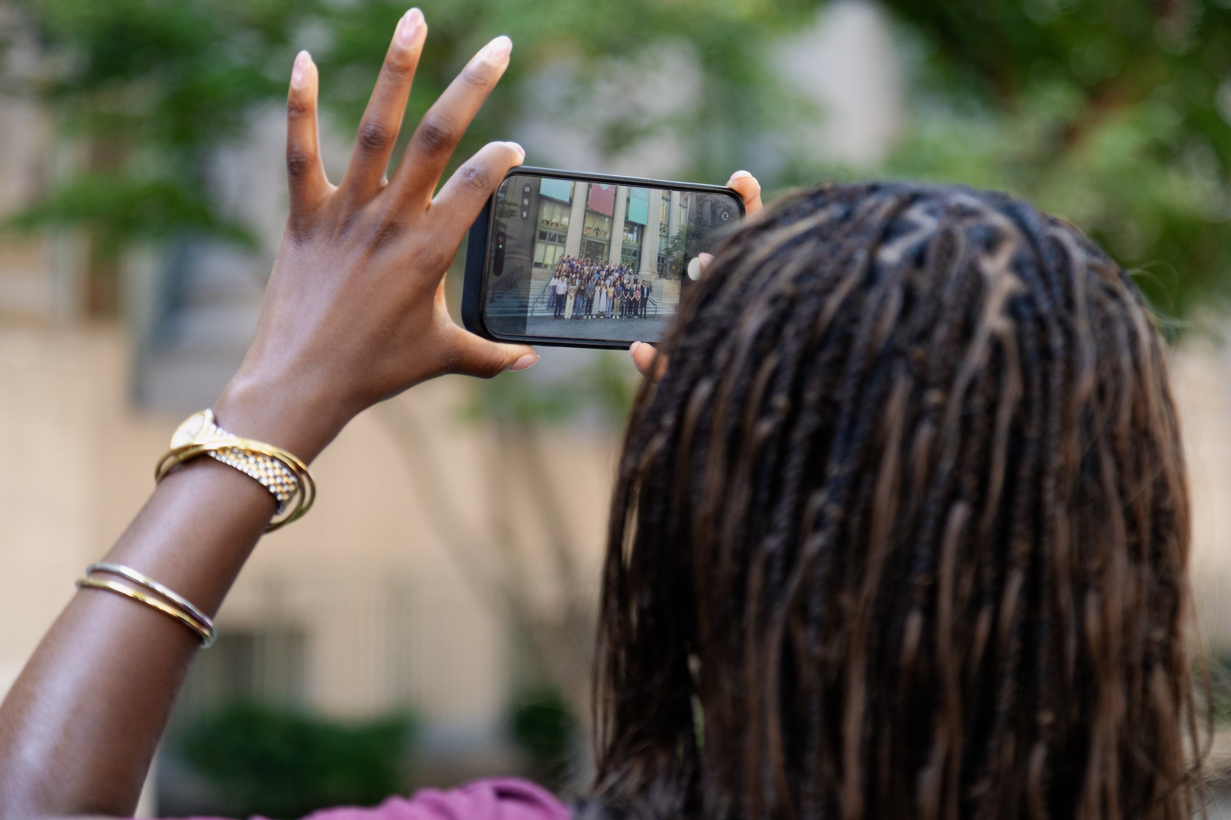 A person holds a smartphone to capture a group photo of people standing outdoors.