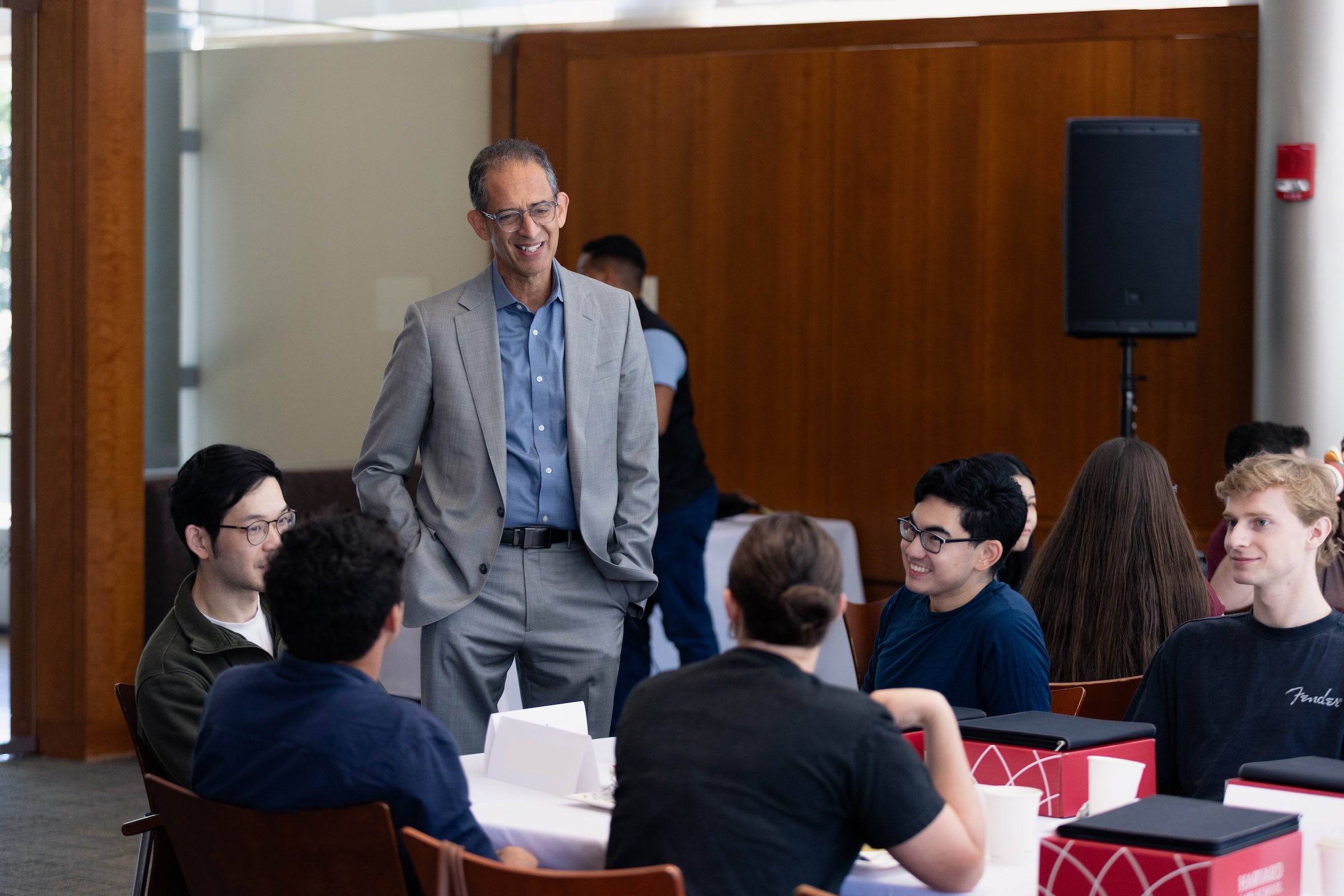 Dean Goldberg smiles and converses with a group of students seated around tables in a conference room.
