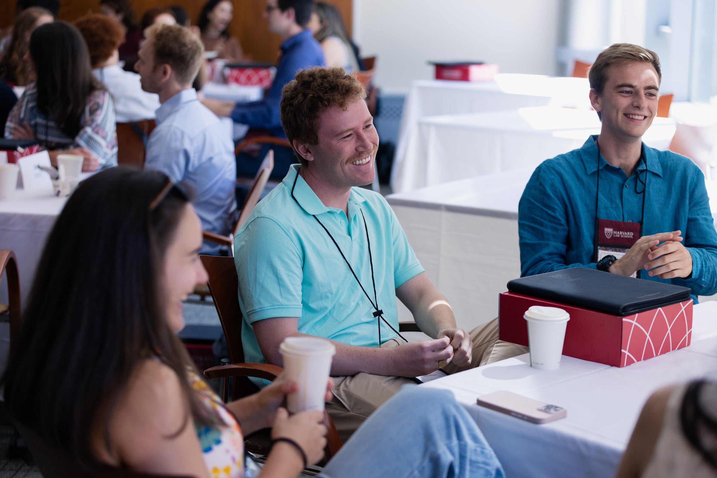 Three students laugh together at a table during a social gathering.