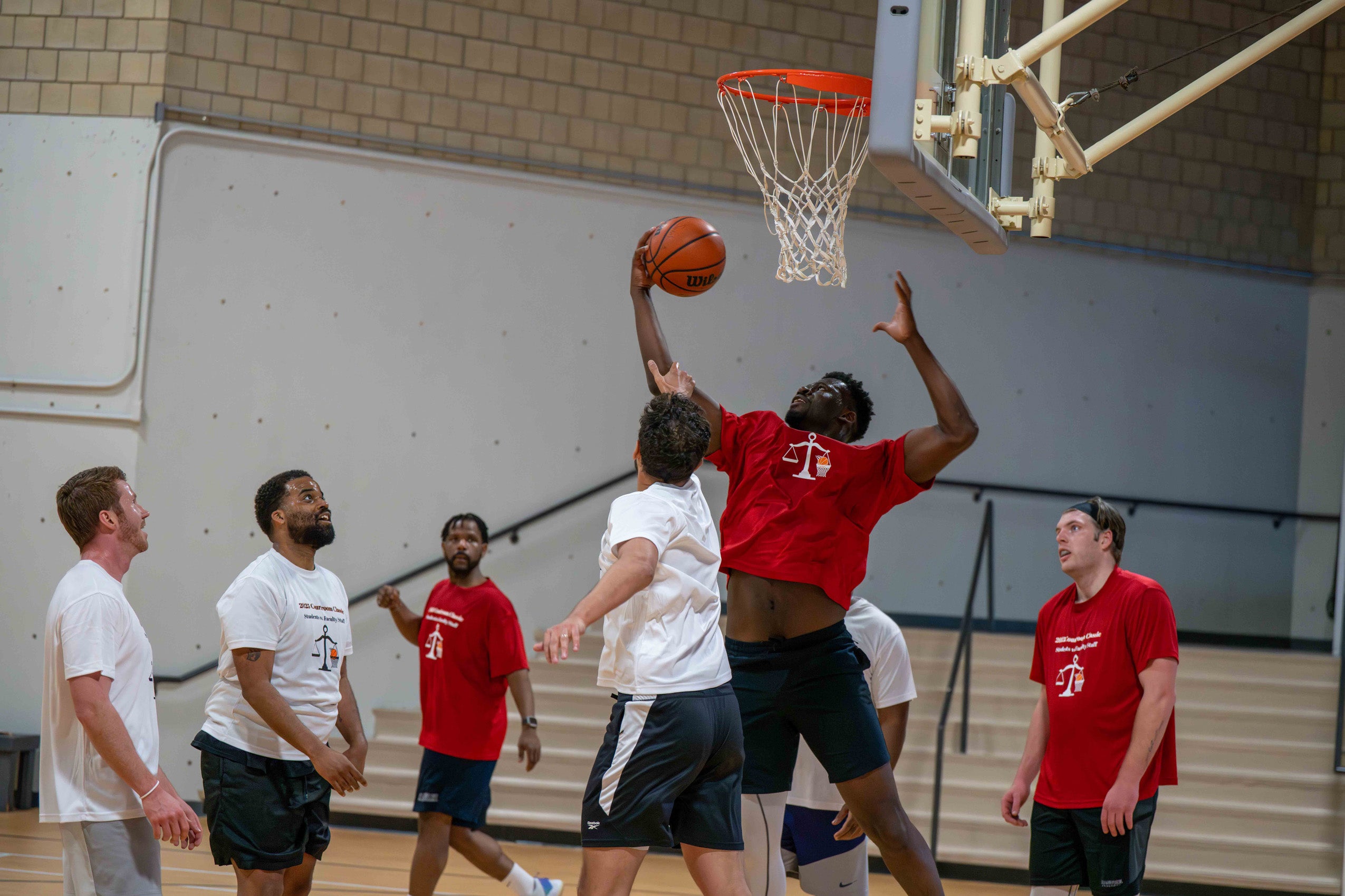 A group of men wearing red or white shirts playing basketball.