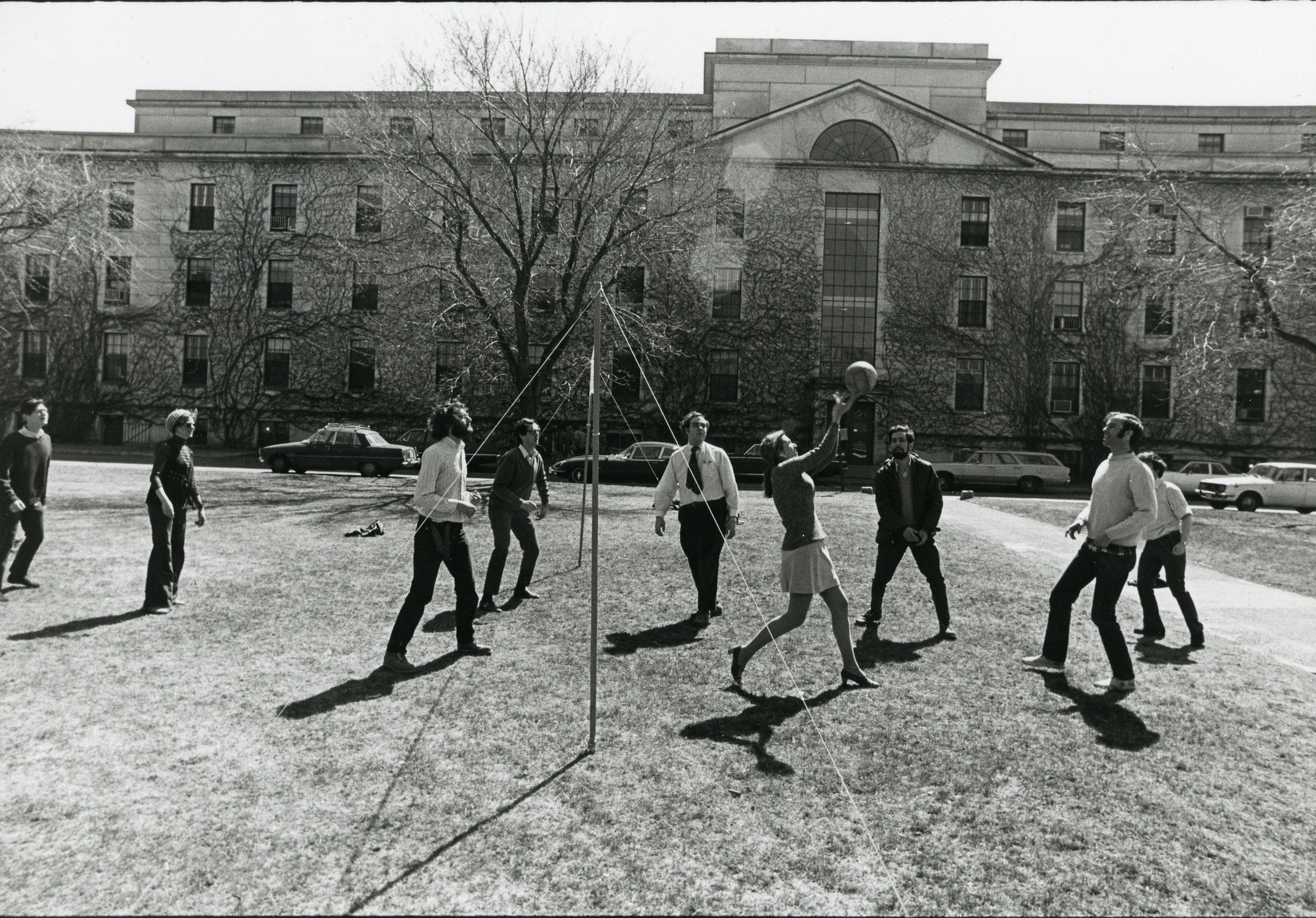 A group of students -- playing volley ball. Some men in ties and woman in a skirt and high heals.